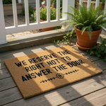 Funny doormat with the text We Reserve The Right Not To Answer The Door, featuring a natural coir fiber welcome mat design with black lettering and a floral accent, perfect for a humorous front porch entry or housewarming home