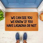 Funny lasagna doormat with bold black text on a natural coir fiber welcome mat, placed at a blue front door entrance for a humorous home decor look that greets guests with a witty food-themed message on a durable outdoor floor