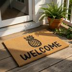 Pineapple welcome doormat featuring a natural coir fiber texture with a bold black pineapple graphic and the word welcome printed in a modern font, perfect for a front porch entry rug or a stylish housewarming home decor accent.
