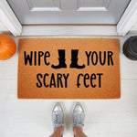 Funny Halloween doormat with Wipe Your Scary Feet text and boot icons, a natural coir fiber welcome mat for fall porch decor, placed on a white front porch with a pumpkin and cauldron for seasonal home entry and entryway floor