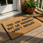 Funny doormat with the text You Can Knock But We Probably Won't Answer printed in bold black letters on a natural coir fiber welcome mat, perfect for a sarcastic front porch decor style that keeps unwanted visitors away from your