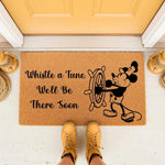 Coir doormat featuring a cartoon mouse steering a ship wheel with the text Whistle a Tune We'll Be There Soon, placed on a porch in front of a yellow door with lanterns, perfect for a fun entryway or outdoor home decor welcome