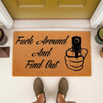 Funny doormat with a hand holding a gun graphic and the text Fuck Around And Find Out, this natural coir fiber welcome mat is a bold front porch decor piece for home entryways that adds a humorous and edgy touch to your outdoor