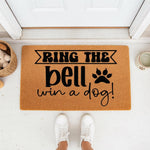 Funny dog lover doormat with text Ring the bell win a dog and a paw print design, featuring a natural coir fiber welcome mat placed on a porch, perfect for pet owners looking for humorous front door decor and unique housewarming