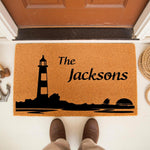 Personalized lighthouse doormat for front porch entry, featuring a nautical coastal design with a black lighthouse silhouette on natural coir fiber, perfect as a custom family name welcome mat for beach house or lake home decor.