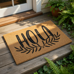 Hola coir doormat with black botanical leaf design, this natural fiber welcome mat features a modern script font and rustic farmhouse style for your front porch entry, creating a stylish and inviting outdoor floor rug for your