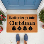 Funny Christmas doormat with balls deep into Christmas text and ornament icons, featuring a natural coir fiber welcome mat on a front porch with holiday decor, perfect for a humorous seasonal home entrance or festive entryway