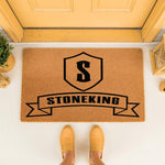 Personalized family name coir doormat featuring a custom shield monogram and banner design, perfect for a front porch entrance.