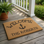 Personalized nautical welcome doormat featuring a black anchor icon and custom family name text on a natural coir fiber mat, perfect for a beach house, coastal home decor, or a front porch entrance for a nautical themed entryway.