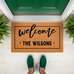 Personalized family name welcome doormat featuring a natural coir fiber texture, black script lettering, and a clean rectangular border, perfect for a front porch entryway or housewarming decor for a new home entrance.