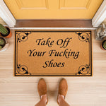 Funny Take Off Your Fucking Shoes doormat featuring a natural coir fiber texture with black scrollwork borders, placed on a porch floor as a rude welcome mat for guests that clearly communicates house rules with blunt humor.