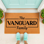 Personalized family name doormat featuring a custom last name in a bold black box design, this natural coir fiber welcome mat sits on a porch floor as a stylish housewarming decor piece for your front door entrance and home