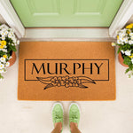 Personalized family name doormat featuring a floral design on natural coir fiber, perfect as a custom front porch welcome mat for home decor, housewarming, or a new home entrance, shown with potted flowers and green sneakers.
