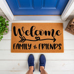 Welcome Family and Friends coir doormat featuring a black arrow and heart design on a natural fiber rug, placed on a white porch in front of a blue door for a stylish home entrance decor look that greets your house guests warmly.