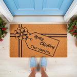 Personalized Merry Christmas doormat with a gift box design and custom family name, featuring a natural coir welcome mat on a porch with festive greenery, perfect for holiday home decor and seasonal front door entrance styling.