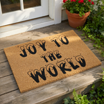 Joy to the World holiday doormat featuring black text with a melting drip effect on a natural coir fiber mat, perfect for a festive front porch entrance or seasonal home decor for your entryway floor during the winter season.