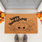 Happy Thanksgiving coir doormat featuring a cute cartoon pumpkin and fall leaves, perfect for autumn porch decor, seasonal entryway rugs, and festive home welcome mats placed outside a front door with pumpkins and gray shoes