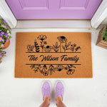 Personalized floral family name doormat featuring a natural coir fiber texture with black botanical line art, placed on a porch in front of a purple door with a person wearing purple sneakers standing on the welcome mat for home