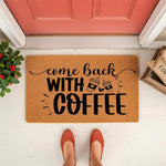 Come Back With Coffee doormat for front porch, a natural fiber welcome mat featuring black script and block lettering with coffee cup icons, placed on a white floor in front of a red door for a fun and inviting home entryway