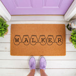 Personalized family name doormat featuring cute mitten illustrations on a natural coir fiber welcome mat, perfect for a front porch entry.