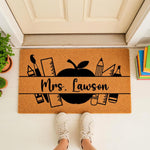 Personalized teacher doormat with school supplies and apple design on a natural coir welcome mat, featuring a custom name area for a classroom entrance or front porch decor, perfect for back to school or teacher appreciation