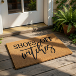 A textured area rug with the phrase "SHOES OFF WITCHES" printed on it in a decorative font.