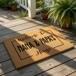 A welcome mat with the text "Welcome To Grammy & Poppaw's House" printed on it, surrounded by greenery and a checkered cloth.