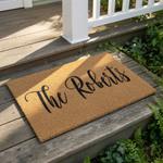 A beige doormat with the name "The Roberts" written on it in a cursive font.