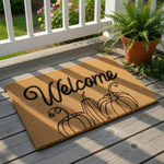 A welcome mat with the word "Welcome" written on it, along with three stylized pumpkins.