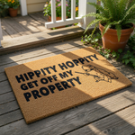 A textured doormat with the text "Hippity Hoppy Get off my Property" printed on it, along with a small illustration of a frog holding a stick.