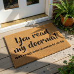 A textured doormat with the text "You read my doormat that's enough social interaction for one day" printed on it.