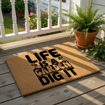 A person holding a sign with the text "LIFE IS A GARDEN DIG IT" in front of a vase of flowers.