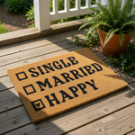 A wooden door mat with the words "SINGLE" and "MARRIED" printed on it, along with the word "HAPPY" below.