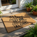 a door mat with a motivational quote, "It's a beautiful day to leave me alone", accompanied by a small potted plant.