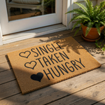 A door mat with the text "SINGLE TAKEN HUNGRY" printed on it, along with a heart symbol and a heart symbol with a heart inside it.