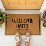 A wooden door mat with the text "WELCOME HOME" printed on it, placed on a tiled floor in front of a green door.