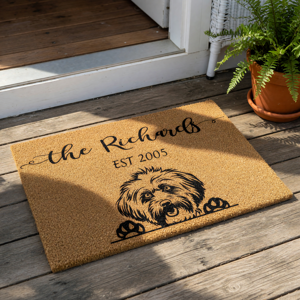 A rectangular, light brown doormat with a black illustration of a dog's head peeking out from behind it.