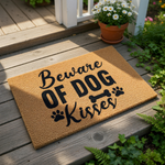 A textured doormat with the phrase "Beware of dog kisses" printed on it, along with paw prints and a bone.