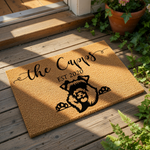 a black and white illustration of a dog with its head sticking out of a doormat, accompanied by the text "the Capris EST 2020" in a decorative font.