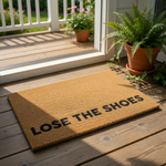 A rectangular, light brown doormat with the text "LOSE THE SHOES" printed on it.