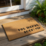 A rectangular, beige-colored doormat with personalized text printed on it.
