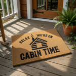 A textured area rug with a black cabin silhouette and the text "Relax, we're on cabin time" printed on it.