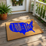 A doormat with a stylized design of the United States of America in blue, with the text "LAND OF THE FREE" written in a bold, decorative font.