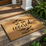 A textured area rug with the text "WE ARE COVERED" and "PSALM 91" printed on it.