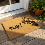 A door mat with a giraffe wearing sunglasses and the text "SUP?" printed on it.
