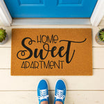 Home Sweet Apartment coir doormat for front porch entry, featuring natural fiber material with black script text, placed on a white floor in front of a blue door for a stylish housewarming or new home decor welcome mat look.