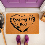 Fishing themed welcome doormat with a heart-shaped rod and reel design, featuring the text Keeping It Reel on a natural coir fiber mat, perfect for a front porch entrance or outdoor home decor for fishing enthusiasts and anglers.
