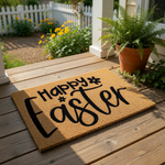 Happy Easter coir doormat featuring black script text on a natural fiber welcome mat, displayed on a front porch wood deck for spring seasonal home decor, perfect for an outdoor entryway or front door entrance floor mat