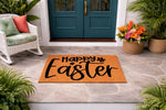 Happy Easter coir doormat for front porch decor, featuring bold black script text on a natural fiber welcome mat, displayed on a stone patio entrance with potted plants and a white wicker chair for seasonal spring home entryway