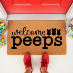 Easter welcome peeps doormat featuring a natural coir fiber texture with black text and bunny silhouettes, placed on a porch with colorful eggs and flowers for a festive spring home decor look that greets guests at the front door.
